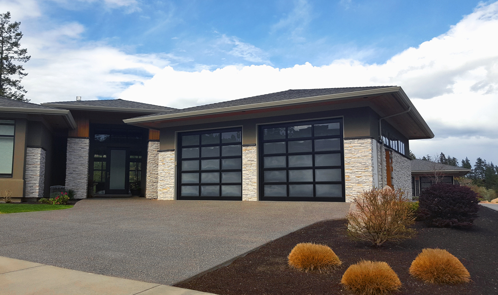 Modern Opaque glass like material on Garage Door of a home. Modern home with stone columns, wood and concrete. Stipple stone driveway up to garage and home.