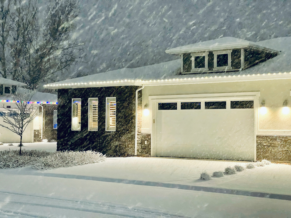 A home with holiday lights in a neighborhood during a snowstorm.